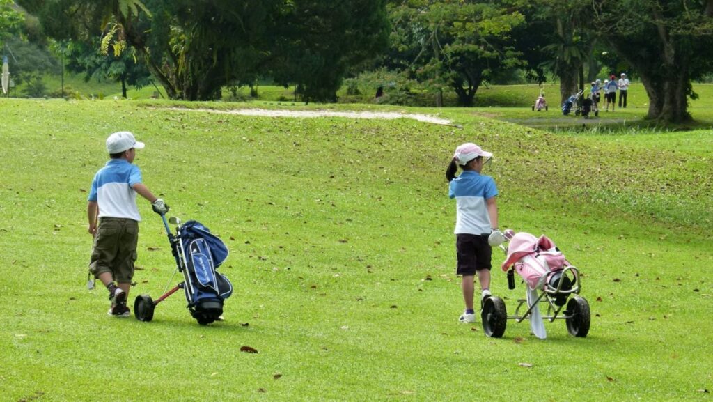 Niños En el campo de golf transportando sus bolsas de palos